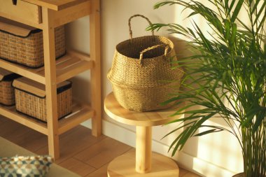 A sunny corner features a wicker basket on a wooden stool beside a plant.