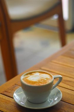 A cup of coffee sits on a wooden table in a quaint cafe setting.