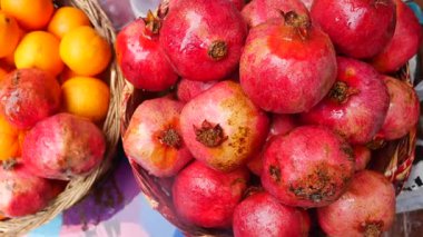 Colorful pomegranates and oranges are displayed at a market stand.