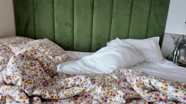 Bedding is rumpled and pillows are scattered in a bright room.