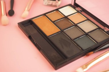 Makyaj paleti pembe bir yüzeyde fırçaların yanında, kullanıma hazır..