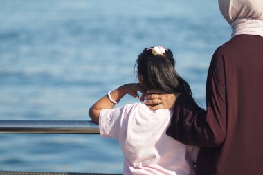 Bir çocuk, bir yetişkin yanında durup bir anı paylaşırken, suyu gözlemler..