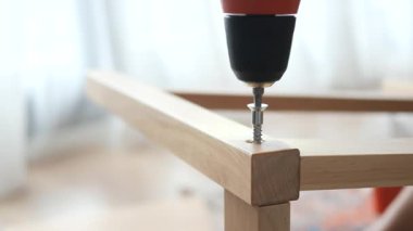 Bir kişi elektrikli matkap ve vidalar kullanarak tahta bir masa kuruyor..