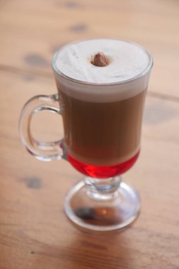 A colorful warm drink with cream on top sits on a wooden table.