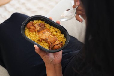 Bir insan rahatça otururken bir tabak tavuk ve pilavın tadını çıkarır..