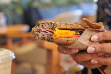 Bir insan kafede et ve peynirle dolu lezzetli bir sandviçin tadını çıkarır..