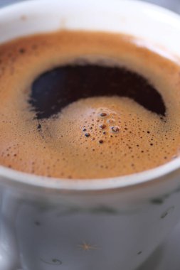 Koyu kahvenin üzerinde beyaz bir fincanda kalın krema şekilleri var..