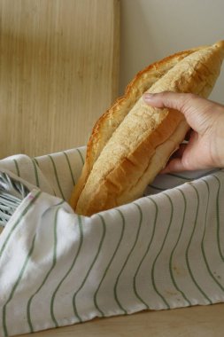 Bir insan mutfaktaki kumaş sepetinden bir somun ekmek alır..