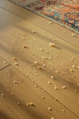 Güneşli bir alanda ahşap bir zemine saçılmış küçük ekmek parçaları..