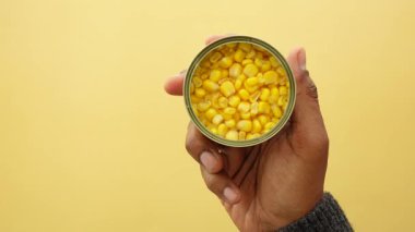 Bir el, parlak sarı mısır taneleriyle dolu açık bir kutu sunar..