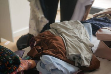 Sıcak bir yatak odasında bir yığın elbiseyi sıralayan bir insan..