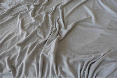 Yumuşak gri bir battaniye, rahat bir görünüm oluşturan bir yatağın üzerine gelişigüzel konur..