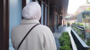 Türbanlı bir kadın yeşillikle kaplı canlı bir şehir sokağında yürüyor..