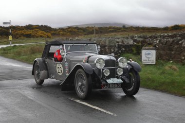 A 1933 Alvis Speed 20 SA leaves Caldbeck, Cumbria.  The car is taking part in the Flying Scotsman Rally, a free public-event. clipart
