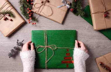 Kadının elinde tahta arka planda hediye kutuları var. Noel ağacı dalları, köknar dalları ve koniler.