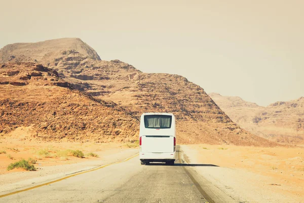 Back view white coach bus drive on asphalt road in scenic Wadi rum mountains in Jordan outdoors take tourist to destination. Cinematic tourism express bus copy space background