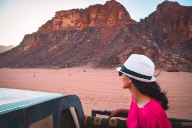 Kadın turist, çölde gün batımı turunda 4wd kamyona binip Wadi romlu doğa koruma alanında çölde oturuyor. Ürdün 'deki kırmızı kumtaşı panoraması yolcuların bakış açısı