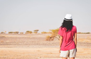 Arkaya bakan dişi turist, Ürdün kırsalının ıssız bir yerinde çölde devenin uzaklığını merak ediyor.