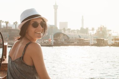 Beyaz kadın turist Dubai 'de tatil yaparken kameraya gülümsüyor. Geleneksel Abra teknesiyle Dubai Deresi 'ne giden bir turist.