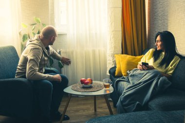 Oturma odasında oturan beyaz bir çift evdeki Avrupa 'daki soğuk evde ısıtma kaloriferlerini kontrol ediyor. Isıtma mevsimi ve ısıtmalı evler