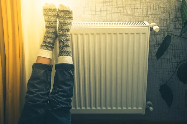 Legs with colorful knitted winter xmas socks on feet warming on central heating radiator heater. Winter time, cold weather season celebrations solitude at home alone