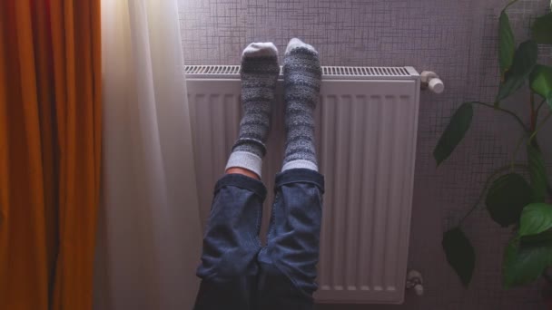 脚上穿着五颜六色的针织冬季圣诞袜的腿在中央暖气散热器上取暖 寒冷的季节 一个人在家里庆祝孤独 — 图库视频影像