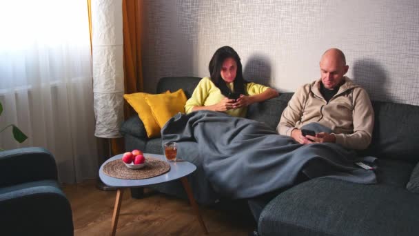 夫妻使用智能手机装置 坐在舒适舒适的沙发公寓上 男友和女友聊天 网上购物 观看滑稽视频 使用社交媒体 流媒体服务 — 图库视频影像