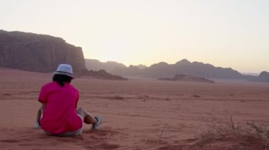 Turist kadın Wadi rom çölünde kumla oynuyor. Dışarıda gün batımını seyrediyor.