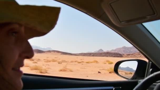 前座景观 高加索女性游客兴奋地从窗口驾驶着具有瓦迪朗姆沙漠背景的租车 在约旦的公路旅行 中东探险 汽车保险和旅行期间到国外度假 — 图库视频影像