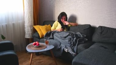 Takım elbiseli Kafkas modern kadın koç parşömenine oturur... akıllı telefondan alışveriş uygulaması yapar... rahat, modern oturma odası evinde tek başına. Evde çalışmanın keyfini çıkar.