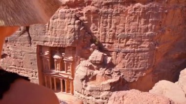 Kafkasyalı turist Petra antik kentinde otururken, Hazine veya Ürdün 'ün ünlü seyahat merkezi olan El Hazine' ye bakıyor. UNESCO Dünya Mirası