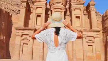 Beyaz elbiseli beyaz kadın turist, Ürdün 'ün Petra kentindeki kayadan oyulmuş bir anıt olan Ad Deir veya El Deir' de beyaz şapka pozuyla poz veriyor. UNESCO Dünya Mirası Alanı