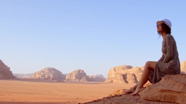 在Wadi Rum沙漠 Wadi Saabit山谷 穿着衣服的女游客赤脚坐在悬崖上观看日出 约旦探索概念 — 图库视频影像