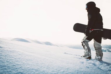 Snowboardcu, gün batımında karlı dağlarda snowboard ile yürüyor. Sinema solo freerider snowboardcusu