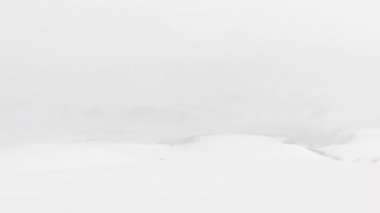 Snowboarder alone in black outfit stand on viewpoint in stormy weather before freeriding downhill. Avalanche dangers and extreme winter weather snow conditions
