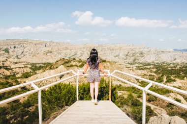 Brunette woman stands on the platform viewpoint and looks left over beautiful landscape of Vashlovani nature reserve