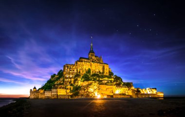 ont Saint-Michel, France night view and starry Milky Way in sky. Built in the XI-XVI centuries. The main facade of the church built in the 12th century. Architect William de Volpiano.