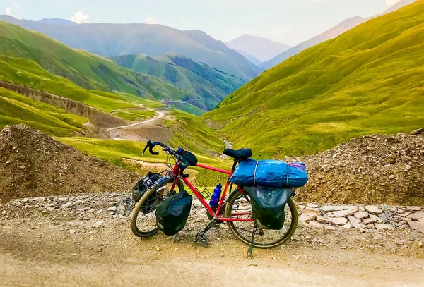 Loaded red touring bicycle with accessories stand in caucasus mountains with beautiful road panorama