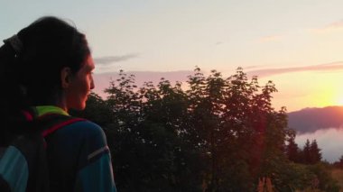 Lonely happy woman portrait watch sunset. Carefree tourist woman looking at sun enjoying landscape. Girl traveler on top of mountain in rays of sunset. Hiker is enjoying nature