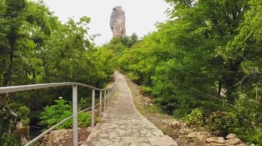 Stone walkway in forest outdoors on hilly terrain with background of Katskhi pillar with iconic church high up on top. Georgian meteora monastery concept.