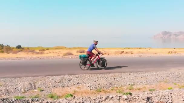 在阳光明媚的夏日 空中侧向跟踪观察年轻的适合高加索男性骑自行车的自行车在风景秀丽的湖畔背景下满载自行车游览 亚美尼亚的积极假日和旅行 — 图库视频影像
