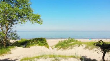 Zoom in view typical Baltic sea coast landscape beach view in Lithuania. Blue sky with no clouds, small waves in the sea and sand dunes partially overgrown with sedge grass