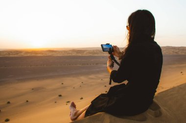 Tourist sit enjoy film experience in desert on sand dune at sunset. Content creator capture moments on sunset in desert outdoors