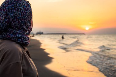 Side view Woman standing on beach alone on sunset looking at seascape landscape. Sunset light, golden hour. Nature and journey concept