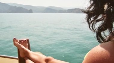 Kafkasyalı kadın, tatil güvertesinde uzanıp kayalık uçurumlarla dolu güneşli Basra Körfezi manzarasının tadını çıkarıyor. Umman tatil beldesi. Mirelas ada turu. Musandam.