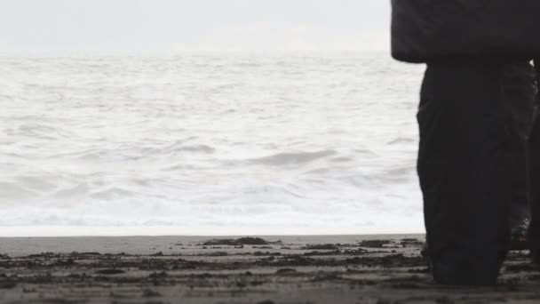 男人和女人穿着靴子 脚踩着黑沙 脚踩着石头 走在海滩上 里尼斯法哈拉海滩游客和运动鞋波浪背景 — 图库视频影像