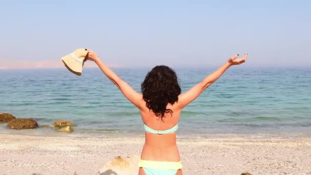 年轻的无忧无虑的高加索女人独自站在碧绿的海滩上兴奋地站着 手举着拖鞋在暑假海滩度假 — 图库视频影像