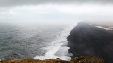 Hava bulutlu bir günde Dyrholaey Burnu, Vik, Güney İzlanda 'dan okyanus siyah volkanik kumlu plajına dramatik bir manzara. Vestmannaeyjar adaları