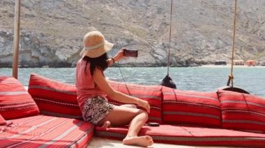 Tatil turnesinde beyaz kadın turist güvertede uzanıp gülümsüyor ve akıllı telefon sevgilisiyle selfie çekiyor.