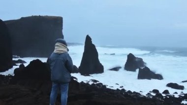 Çok rüzgarlı bir günde, İzlanda 'nın Reykjanes yarımadasındaki kayalara çarpan Atlantik Okyanusu' nu seyreden kadın turist. Popüler manzaralı doğa konumu. Iconic Valahnukamol yığını